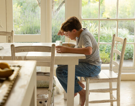 portrait of 13 year old boy eating a bowl of spaghetti in his kitchen