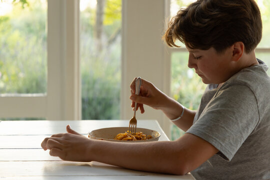 portrait of 13 year old boy eating a bowl of spaghetti in his kitchen