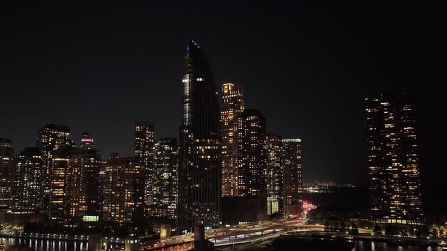Aerial view of illuminated Chicago skyscrapers at night with light trails from highway traffic and dark Lake Michigan beyond, October 6, 2026