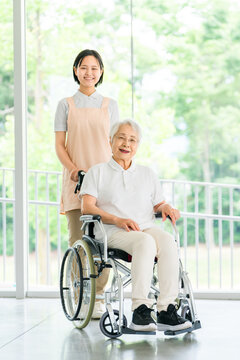 Gray-haired senior woman in a wheelchair being assisted by a caregiver