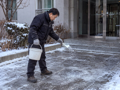 Apartment caretaker spreading deicer outside the entrance