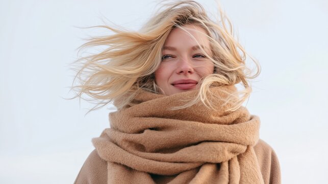 Blonde woman enjoying strong wind blowing hair across her face, feeling fresh and cozy in a thick beige scarf