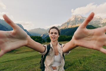 Fototapeta premium A young woman in casual clothes stretches her arms forward smiling in a green mountain meadow under a blue sky. Concept for lifestyle, nature, and freedom.