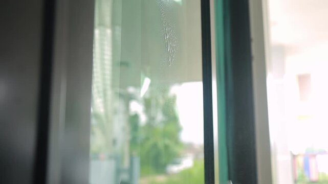 Hand spraying cleaner and wiping a glass window with a cloth