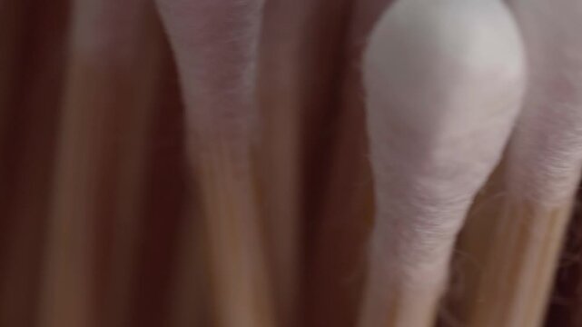 Extreme close up of cotton buds arranged side by side with soft white cotton tips and pale stems filling the frame against a warm brown background with gentle lighting and muted tones.