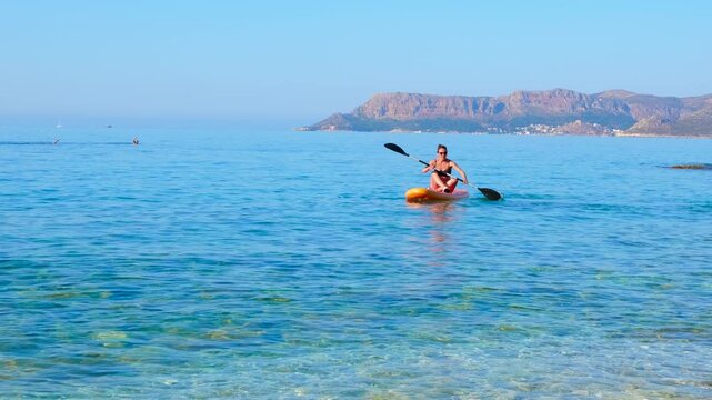 Woman paddleboard on crystal clear turquoise sea. Athletic woman in a bikini paddling her paddleboard on the calm, turquoise sea during a sunny summer day, enjoying an active vacation