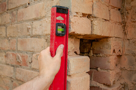 Construction worker uses a level to check the alignment of a damaged brick wall