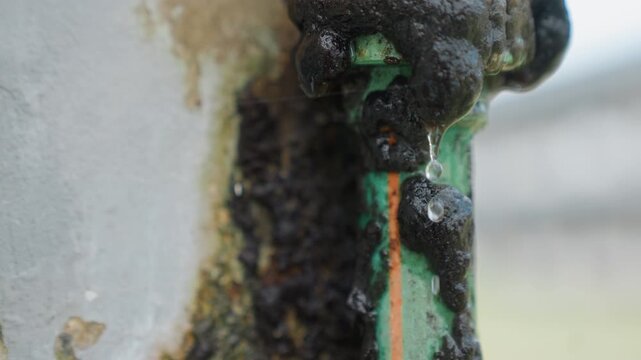Close up shows leaking pipes with dripping liquid focusing on damaged plumbing details against out of focus background leak pipe drip water black substance