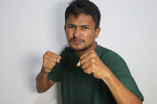Angry young man raising fists in a defensive fighting stance against a plain white wall
