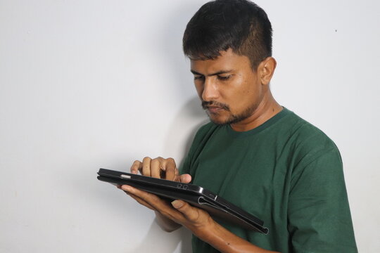 Young man in green shirt using a digital tablet against white wall