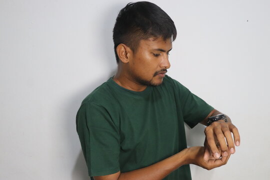 Young man looking at his wristwatch wearing green t shirt indoors