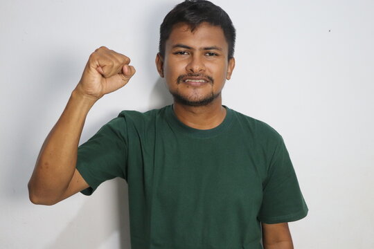Young man raising his clenched fist with confidence wearing a green shirt