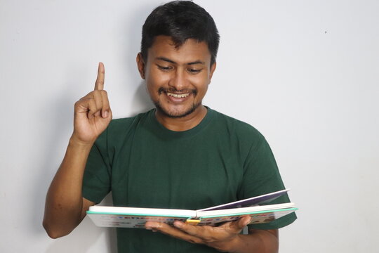 Young man reading a book and raising index finger having an idea
