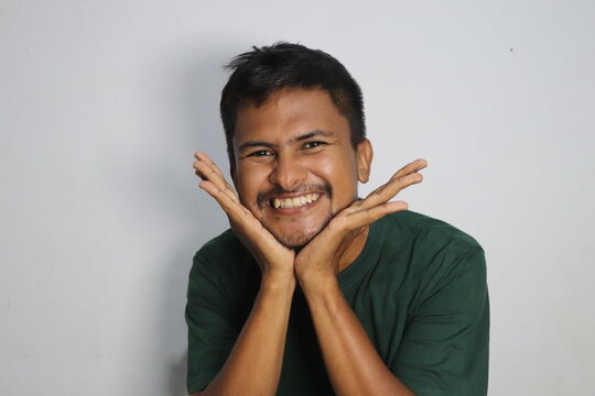 Young man smiling and resting his chin on his hands against a white wall