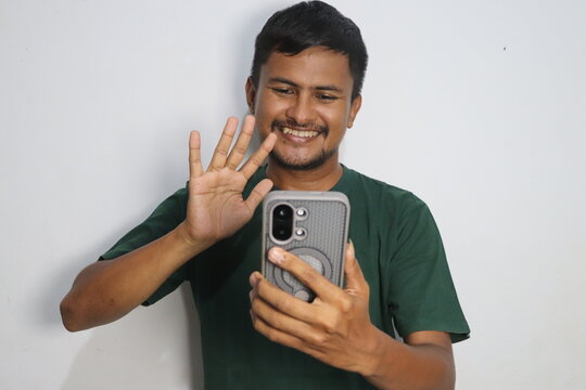 Young man smiling and waving hand during a video call on his smartphone against a plain white background