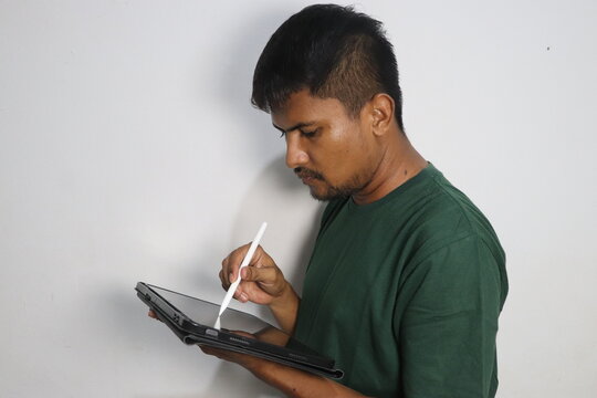 Young man using a digital stylus on a tablet computer against a wall