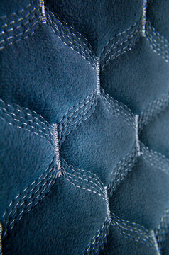 A detailed macro close-up of a blue quilted textile fabric featuring an intricate geometric pattern with silver stitched lines.