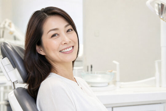 歯科クリニックのチェアで歯科医を見上げ微笑む中年女性患者