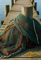 Fototapeta premium Commercial fishing and maritime industry, green and brown fishing net draped over a wooden piling on a weathered pier at a harbor during the day