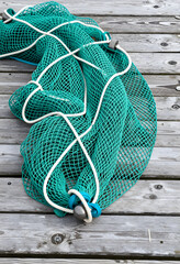 Fototapeta premium Sustainable fishing and marine conservation, green commercial fishing net with weights on a weathered wooden dock for maritime industry and ocean safety