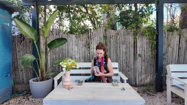 Woman shuffles tarot cards at a table in a garden patio