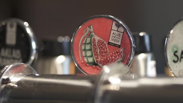 Close up of brewery tap with pomegranate illustration and Alus Daritava Viedi label among polished beer taps in a bar setting