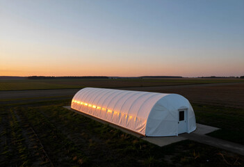 Fototapeta premium Sustainable agriculture and food security, greenhouse tunnel in rural farmland at sunset for organic farming and crop production in a countryside field