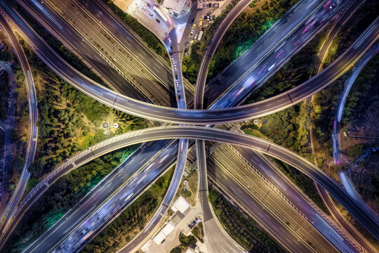 Aerial overhead view of a illuminated, big highway junction with flyover, geometric crossroads and car traffic as aurban transport concept