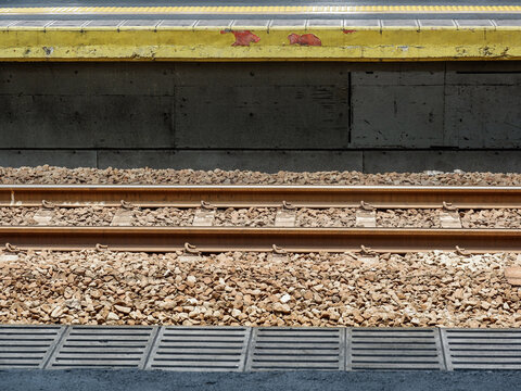 Side view of train station tracks, ballast gravel bed, and concrete platform edge with tactile warning tiles.