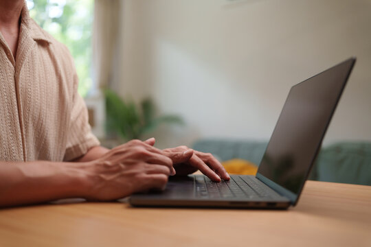 Asian man typing on a laptop at home setting, capturing remote work, digital productivity and a flexible modern workplace.