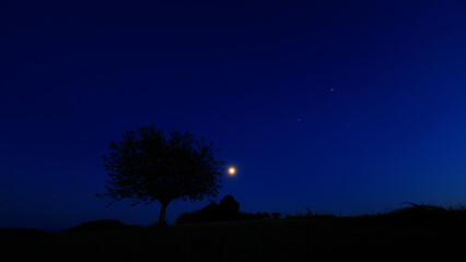 Fototapeta premium Moon on a twilight sky with stars, planets and landscape mountain silhouettes.