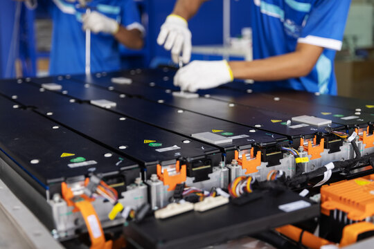 Technicians wearing gloves use hand tools to assemble an electric vehicle battery pack, showing battery modules.