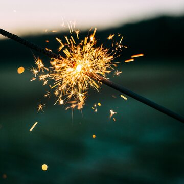 Close up of a burning festive sparkler stick emitting bright golden sparks outdoors during a twilight celebration
