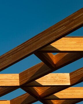 Modern architectural detail of engineered wooden roof trusses and interlocking timber beams against a clear blue sky