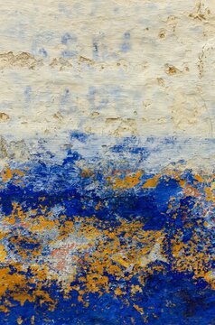 Abstract background of an old weathered concrete wall with peeling layers of white blue and yellow paint showing cracked texture