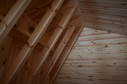 Interior view of exposed wooden roof trusses and timber cladding on an attic ceiling under construction inside a residential house
