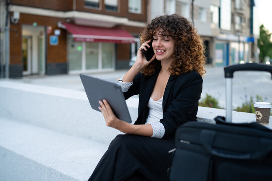 Business white woman using tablet and phone while waiting outdoors