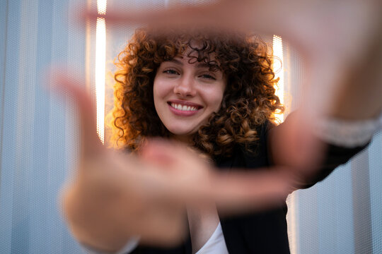 Smiling white woman with curly hair reaches toward camera