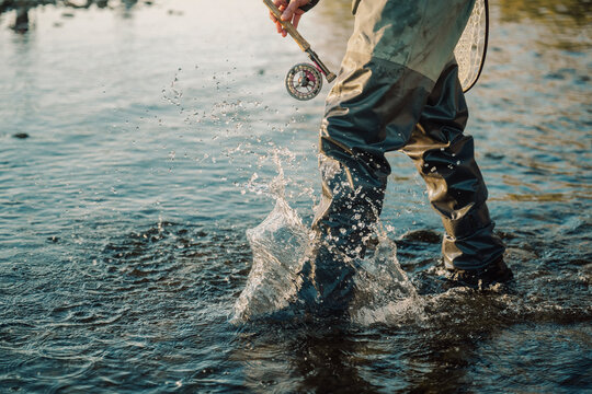 Fly fisherman splashes through shallow river water at sunset.