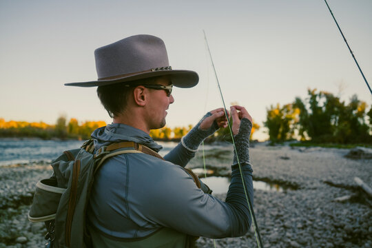 Fly fisherman prepares his line beside a rocky riverbank.