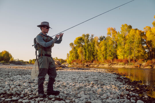 Fly fisherman prepares his rod beside a shallow river.