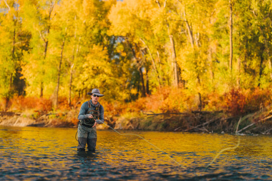 Fly fisherman casts across a river surrounded by vivid autumn leaves.