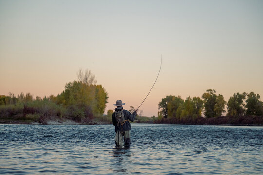 Fly fisherman casts a long line across a wide river at dusk.