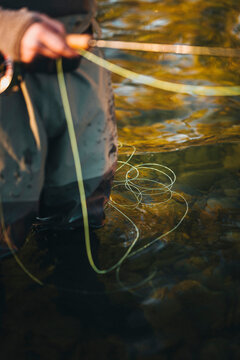 Fly fishing line coils across clear river water beside an angler.