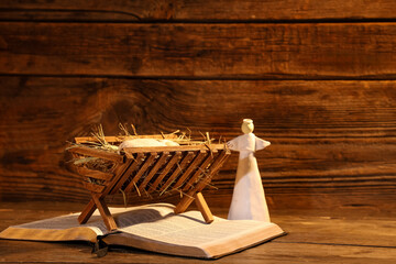 Fototapeta premium Manger with baby Jesus, Holy Bible and angel on wooden table