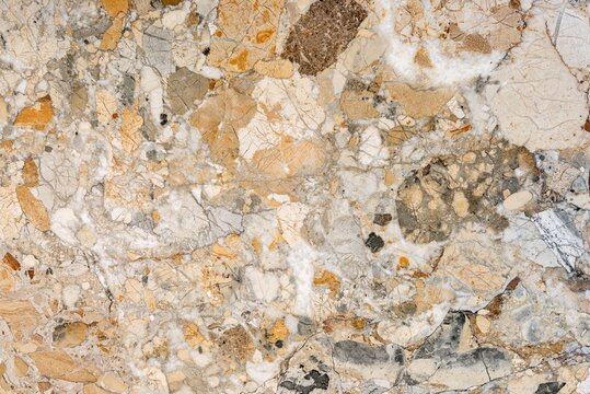 Detailed texture of a polished conglomerate stone surface showing embedded natural pebbles fragments and mineral veins in warm tones