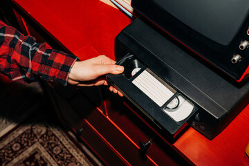 female hand inserts a VHS tape into a VCR, evoking a sense of nostalgia and memories while preparing to watch old home videos from the 90s