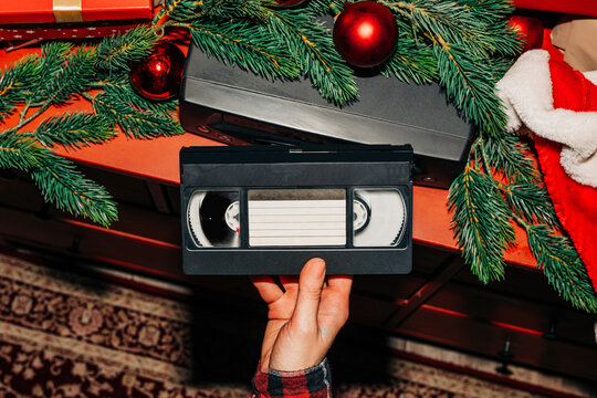 female hand inserts a Christmas-themed VHS tape into a VCR decorated with fir branches and a red bauble, ready to watch nostalgic home videos from the 90s