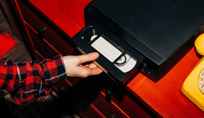 female hand inserts a VHS tape into a VCR, evoking a sense of nostalgia and memories while...