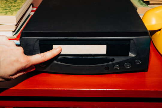 female hand inserts a VHS tape into a VCR, evoking a sense of nostalgia and memories while preparing to watch old home videos from the 90s